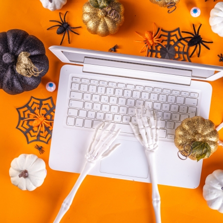 Skeleton hands on a computer with pumpkins surrounding