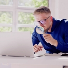 man looking at computer with magnifying glass