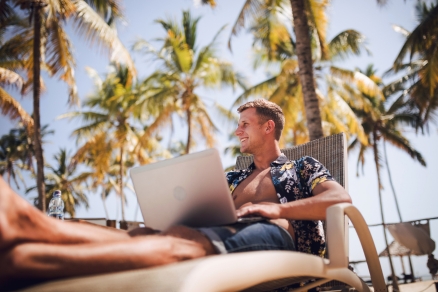 man with computer surrounded by palm trees
