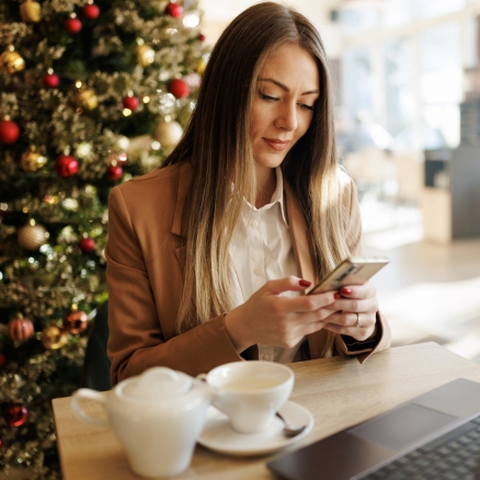 Woman looking at phone with christmas tree behind her