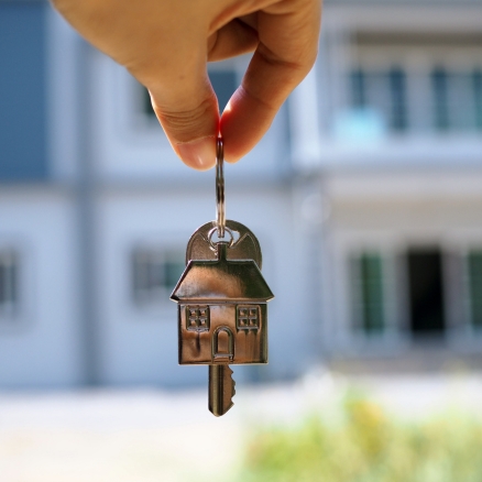 Keys with metal house being  held in front of a house